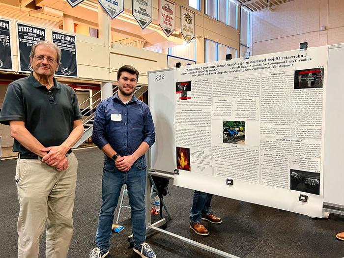 Student and professor stand next to research poster